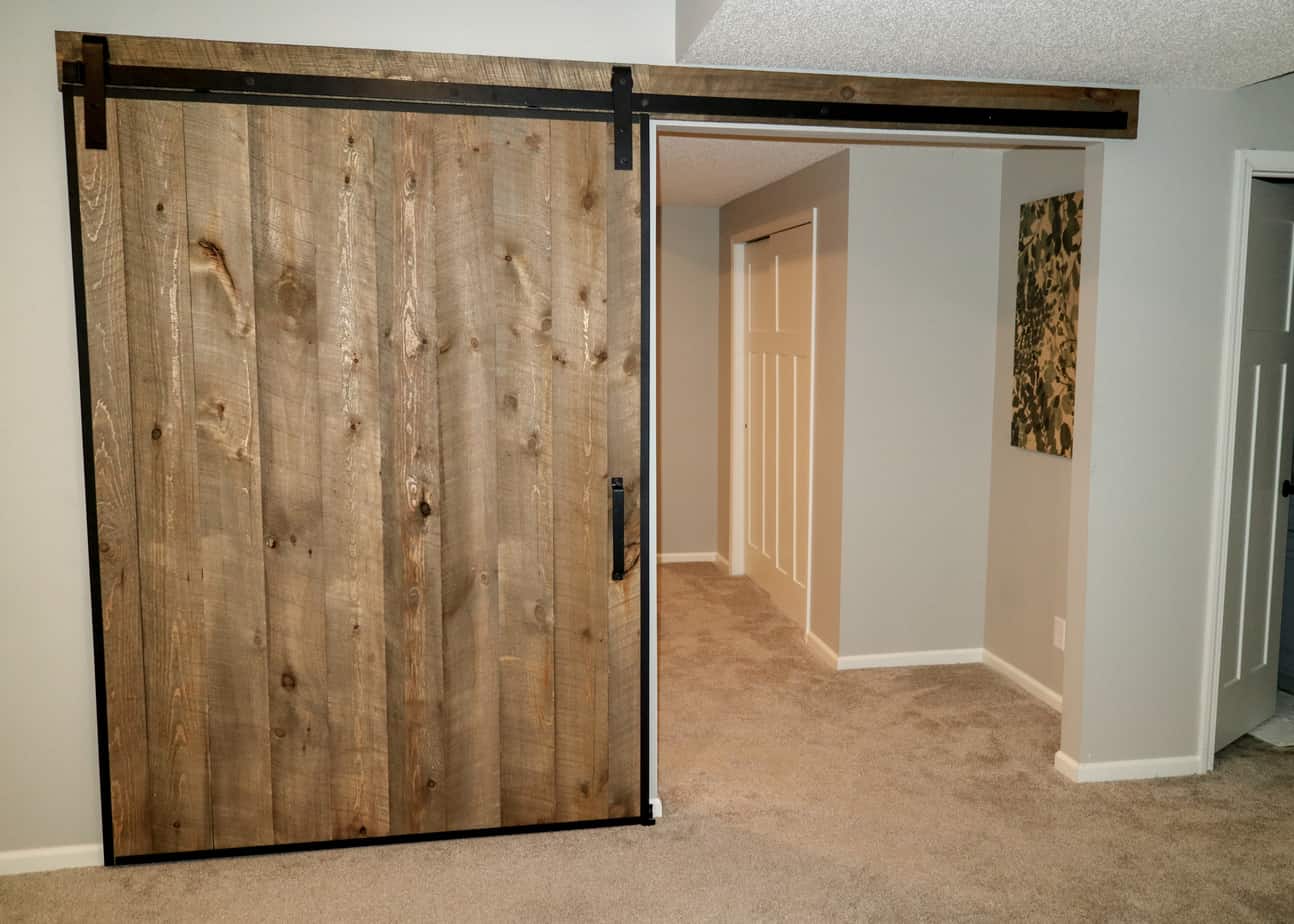 A wood slat barn door framed with Goldberg Brothers barn door edge wrap and mounted to the wall with Goldberg Brothers Standard Series barn door hardware